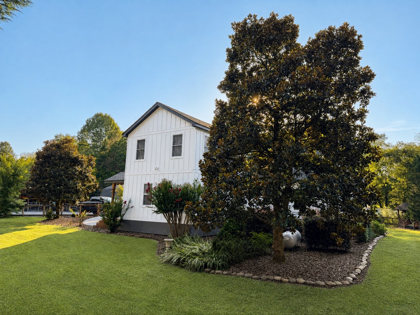 Side elevation of the home bordered by mature trees and planting beds