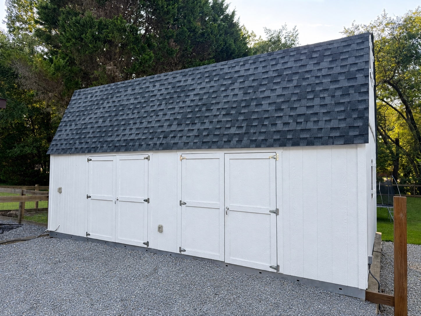 White multi-door storage building beneath mature shade trees