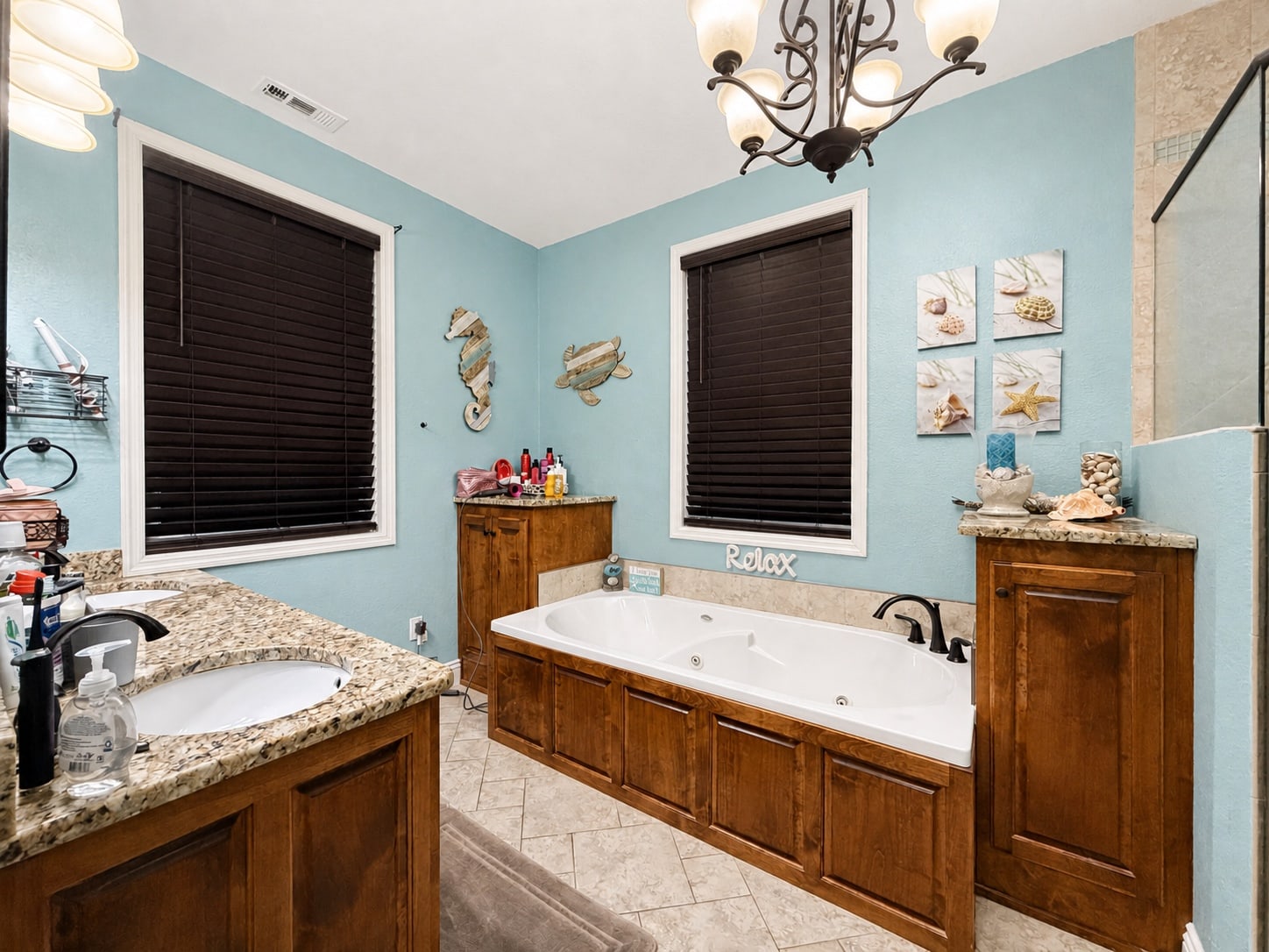 Primary bathroom with jetted tub, wood cabinetry, and granite vanity