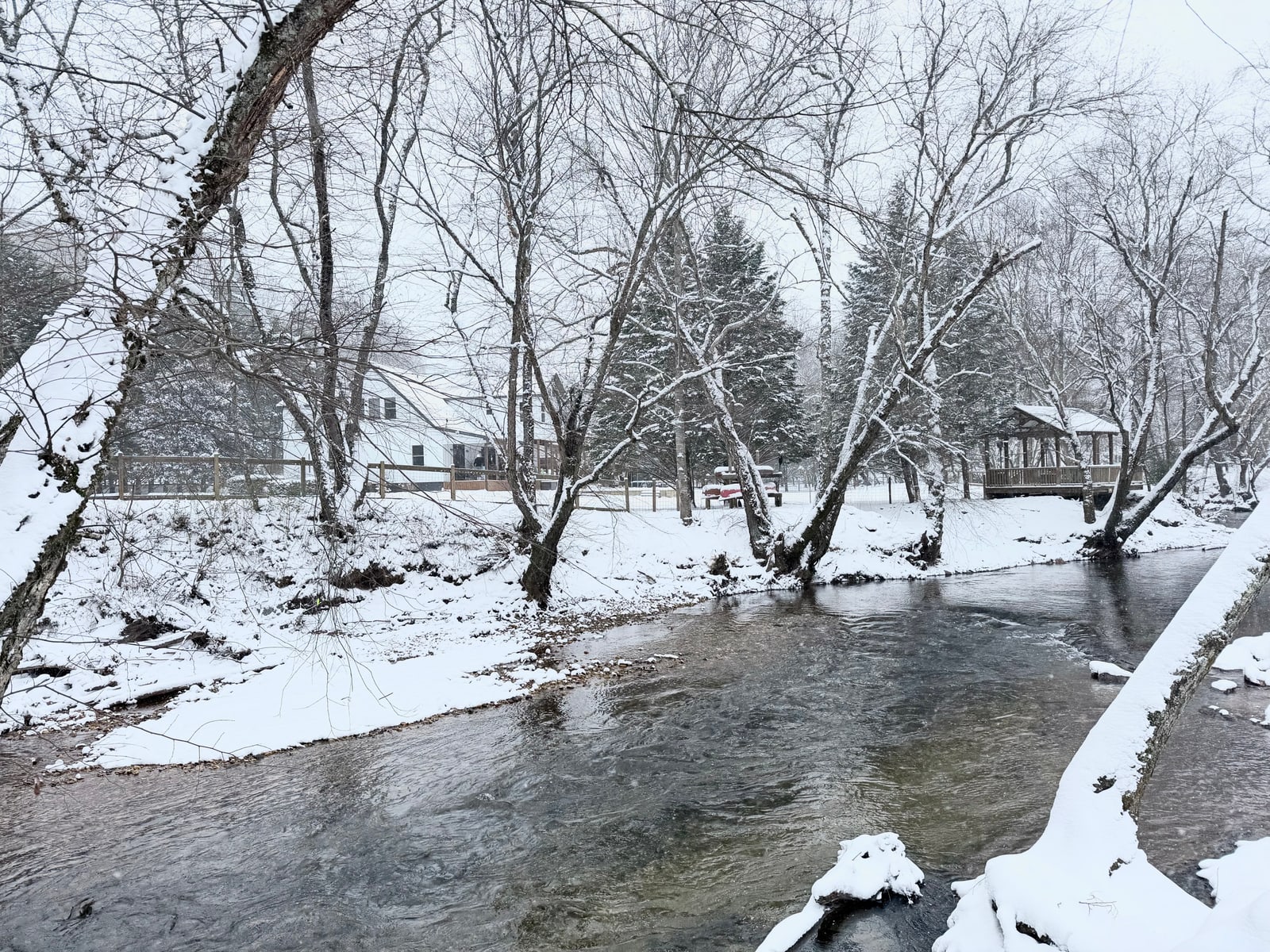 Snow-covered riverfront with the home and gazebo among the trees