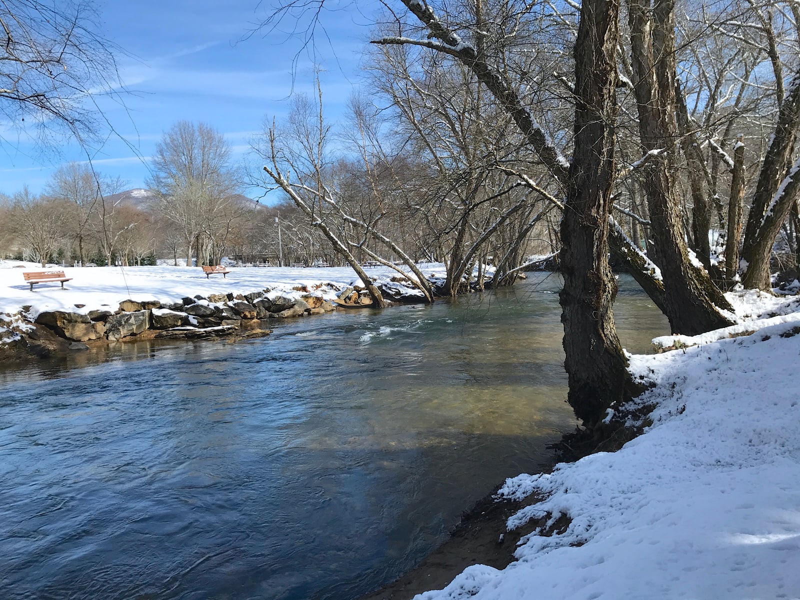 Sunlit winter river with snow-covered banks and a mountain beyond